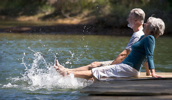 A retired couple relaxing on a dock splashing water, enjoying life with confidence thanks a trusted partnership with BOK.